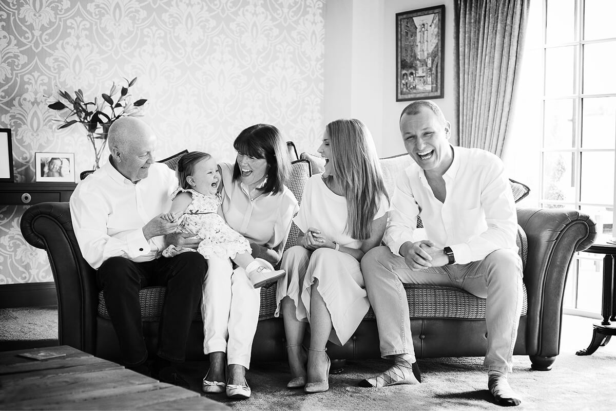 B&W photo of grandparents and mum and dad with their first grandchild on a leather sofa