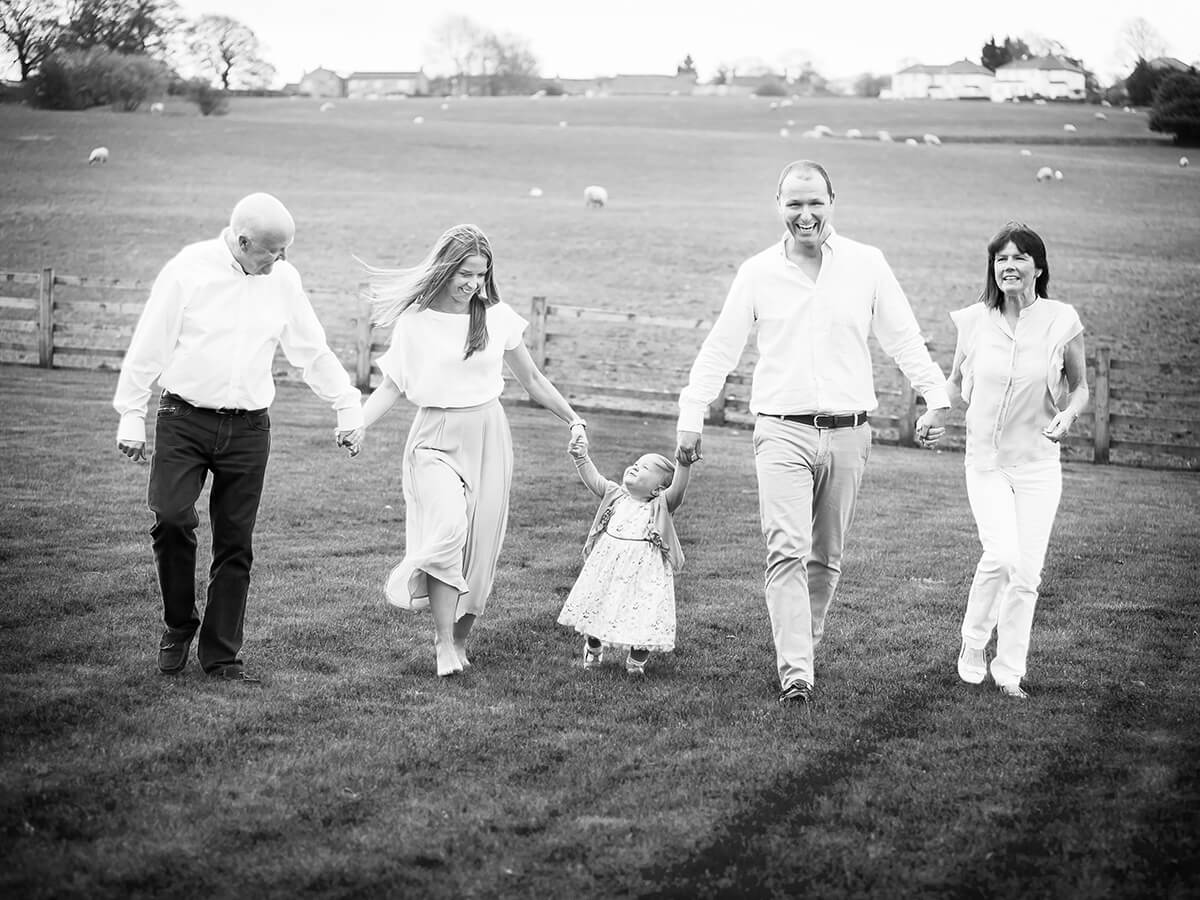 B&W extended family photograph of a beautiful family walking through their garden with a toddler in the middle